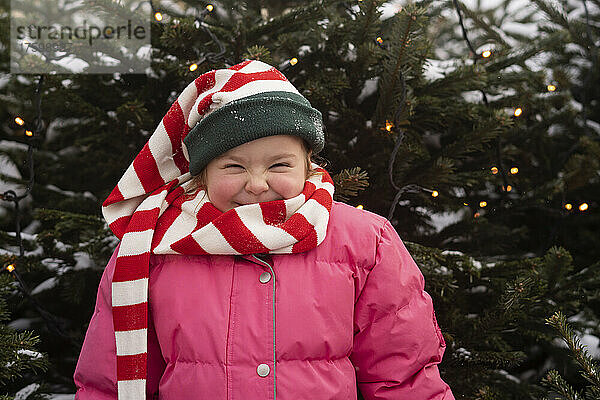 Glückliches Mädchen mit gestreiftem Schal  das vor dem Weihnachtsbaum steht