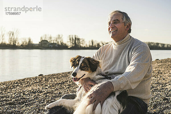 Happy man with dog sitting at beach on sunny day