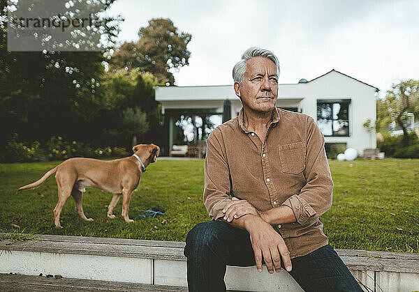 Nachdenklicher älterer Mann mit weißen Haaren sitzt neben einem Hund im Hinterhof