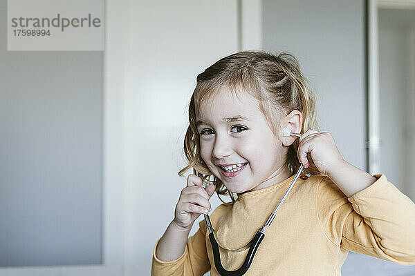 Happy cute blond girl playing with stethoscope at home