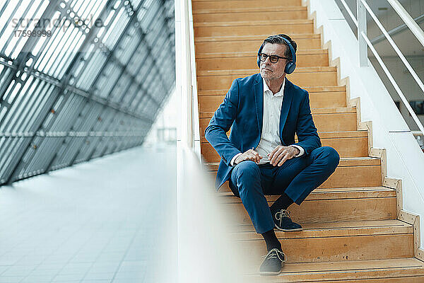 Geschäftsmann mit Kopfhörern sitzt auf Stufen im Büro