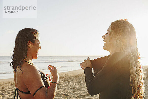 Glückliche Frauen ziehen ihren Neoprenanzug aus  nachdem sie bei Sonnenuntergang am Strand auf Gran Canaria  Kanarische Inseln  gesurft sind