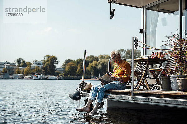 Älterer Mann liest Zeitung und sitzt an einem sonnigen Tag auf dem Hausboot