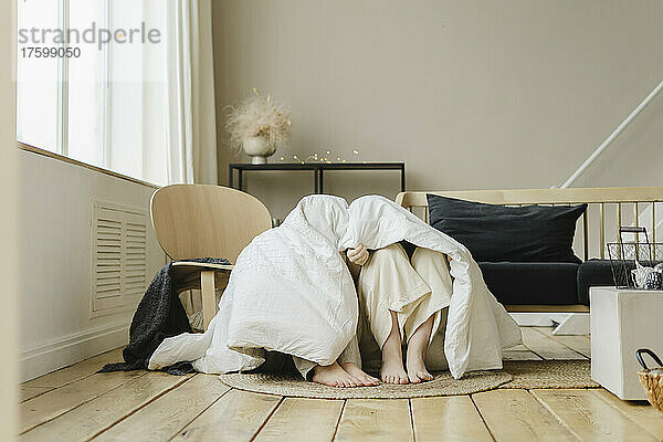 Vorpubertäre Freunde verstecken sich unter einer Decke im Wohnzimmer