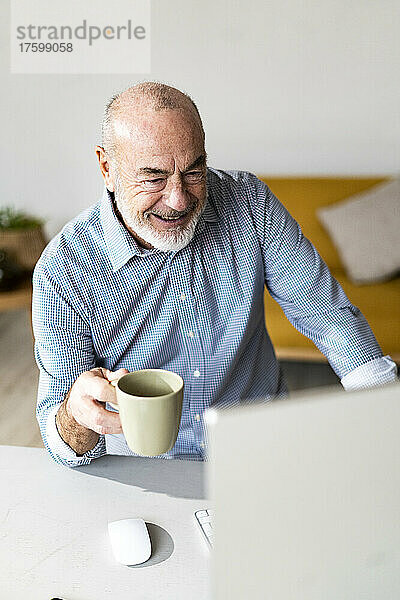 Glücklicher leitender Freiberufler mit Kaffeetasse  der im Heimbüro arbeitet