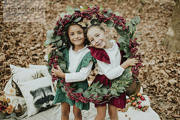 Smiling girls holding Christmas wreath in autumn forest