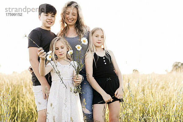 Mädchen hält Blumen mit Familie im Hintergrund im Feld