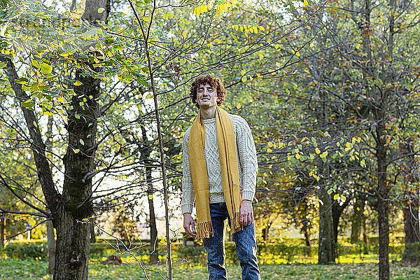 Junger Mann mit gelbem Schal steht im Herbstpark
