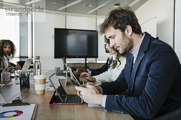 Geschäftsmann benutzt Smartphone und sitzt neben Kollegen am Schreibtisch im Büro