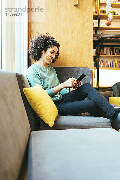 Happy businesswoman text messaging on smart phone on sofa