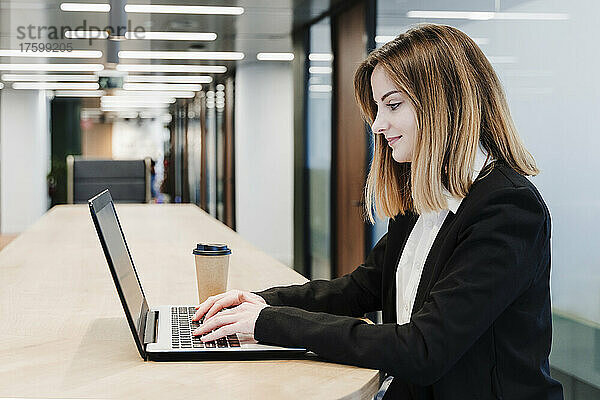 Lächelnde Geschäftsfrau benutzt Laptop auf dem Tisch im Büro