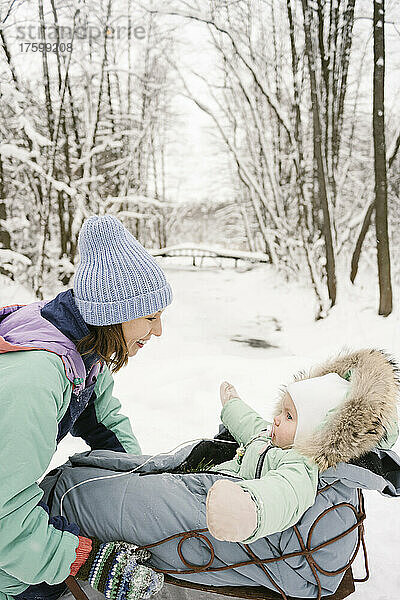 Lächelnde Frau schaut Tochter im Winter auf Schlitten an
