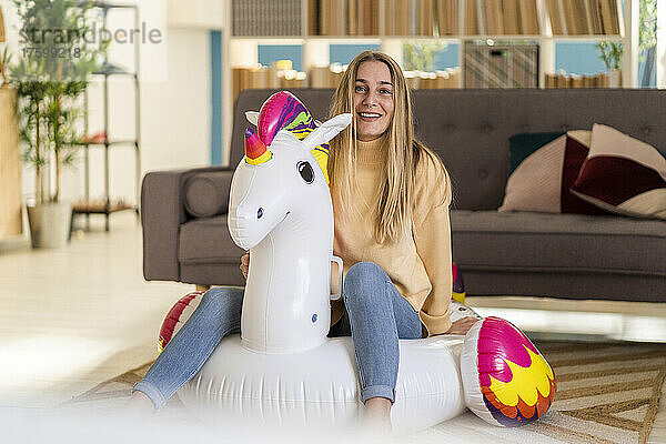Smiling woman sitting on inflatable unicorn in living room