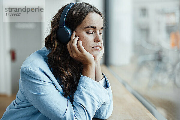 Geschäftsfrau mit geschlossenen Augen hört im Büro Musik über kabellose Kopfhörer