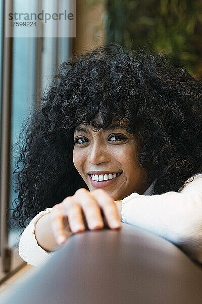 Smiling curly haired woman leaning on sofa at cafe