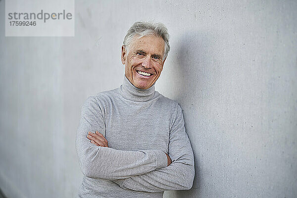Happy elderly man with arms crossed by gray wall