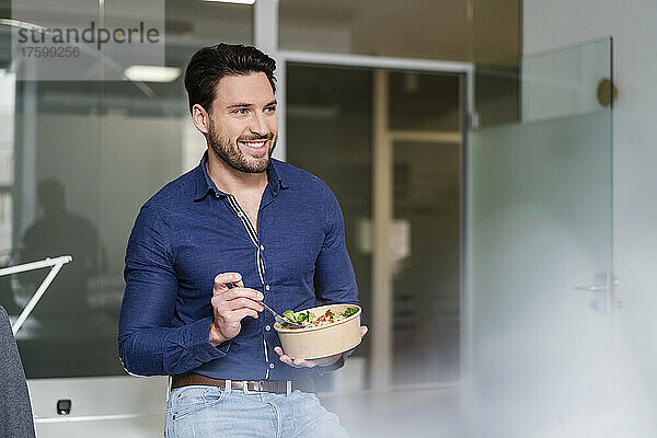 Lächelnder Geschäftsmann mit Salatschüssel macht Pause im Büro