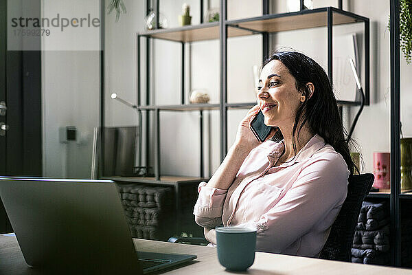 Lächelnde Geschäftsfrau  die im Coworking-Büro mit dem Mobiltelefon spricht