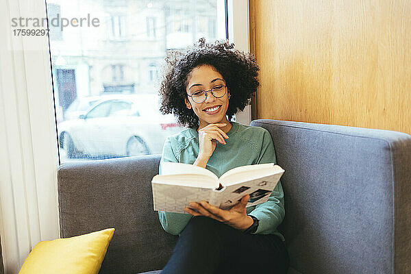 Lächelnde Frau liest ein Buch auf dem Sofa