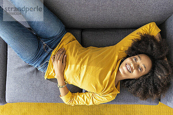 Smiling young woman lying on sofa at home