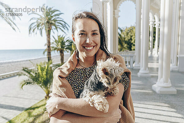 Lächelnde junge Frau mit Hund am Strand