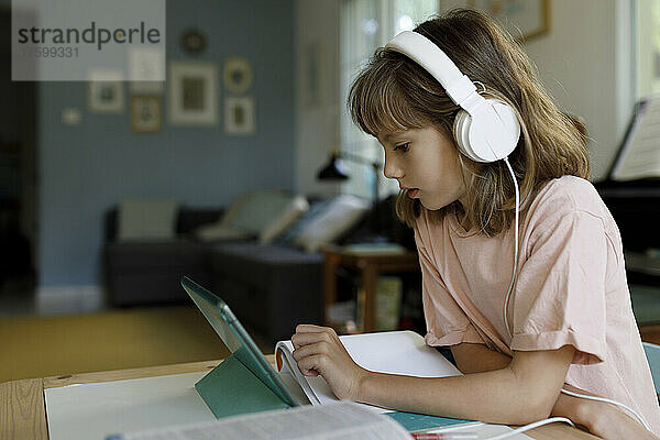 Blondes Mädchen mit Kopfhörern lernt zu Hause über Tablet-PC