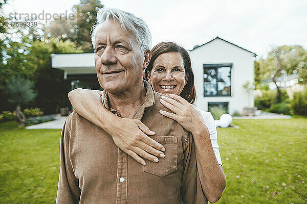 Glückliche Frau umarmt älteren Mann von hinten im Hinterhof