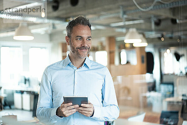 Smiling businessman standing with tablet computer at workplace