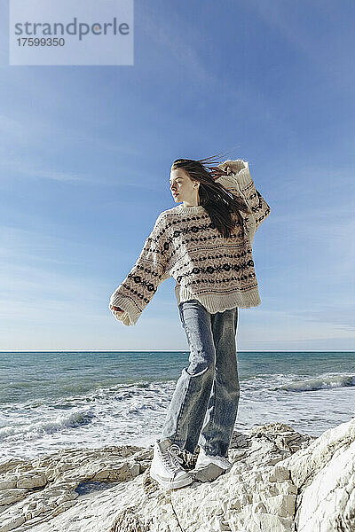 Teenage girl in sweater standing on rock at beach