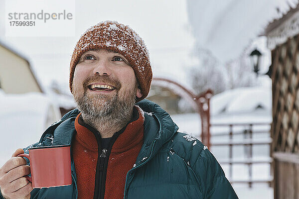 Glücklicher Mann mit Kaffeetasse und Blick nach oben im Winter