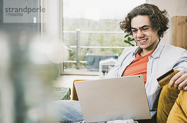 Glücklicher Mann mit Kreditkarte beim Online-Einkauf per Laptop zu Hause