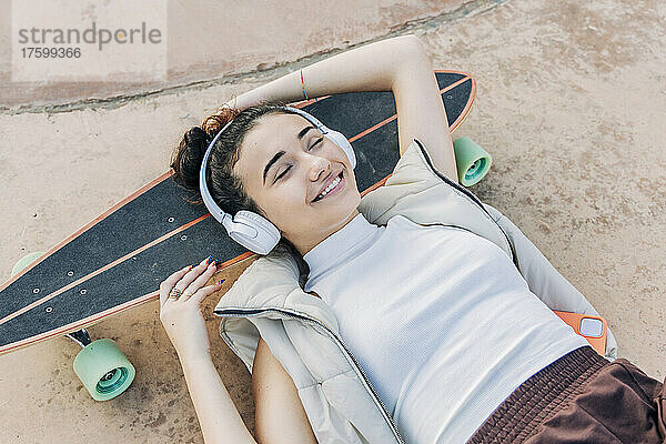 Lächelnde Frau mit Kopfhörern entspannt sich auf dem Skateboard im Park