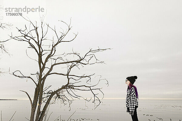 Mädchen blickt im Winter auf kahlen Baum