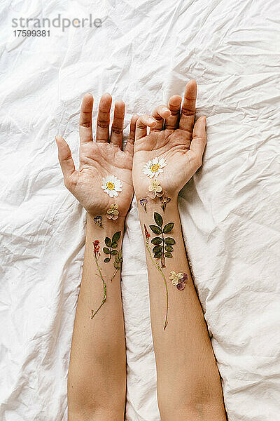 Frauenhände mit Blumen und Zweigen auf dem Bett