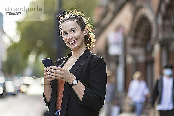 Glückliche Geschäftsfrau mit Smartphone auf der Stadtstraße