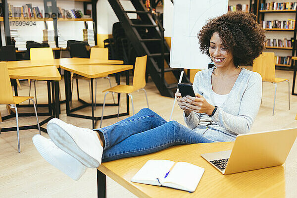 Lächelnde Geschäftsfrau  die am Schreibtisch im Kreativbüro SMS auf dem Smartphone schreibt