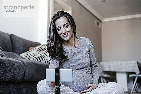 Lächelnde schwangere Frau schaut sich zu Hause das Home-Workout-Tutorial an