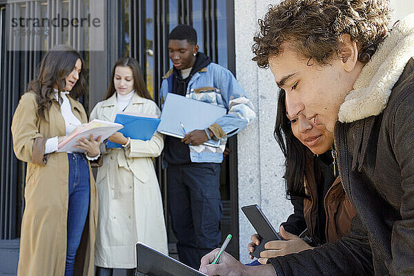 Studenten nutzen Tablet-PC mit Freunden  die im Hintergrund auf dem Universitätscampus studieren