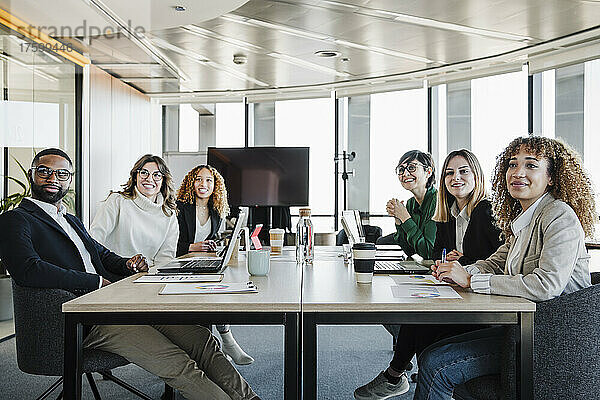 Lächelnde Geschäftsleute und Geschäftsfrauen sitzen bei einer Besprechung am Konferenztisch