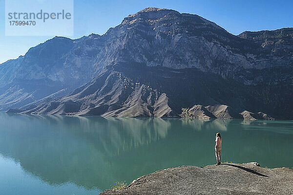 Lone woman admiring mountain lake from nearby ledge