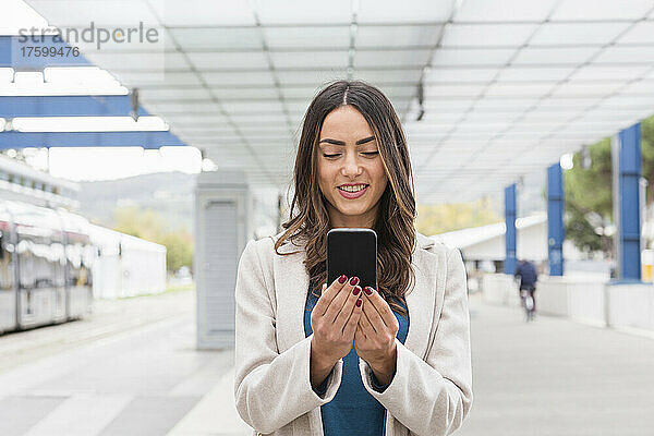 Lächelnde Geschäftsfrau benutzt Mobiltelefon an Straßenbahnhaltestelle