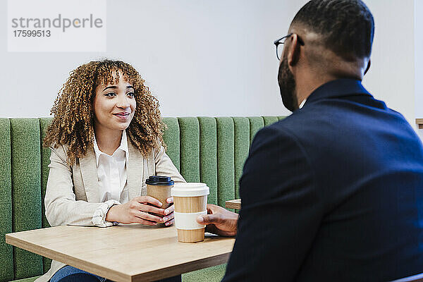 Lächelnde Geschäftsfrau schaut Kollegen bei der Kaffeepause im Coworking-Büro an