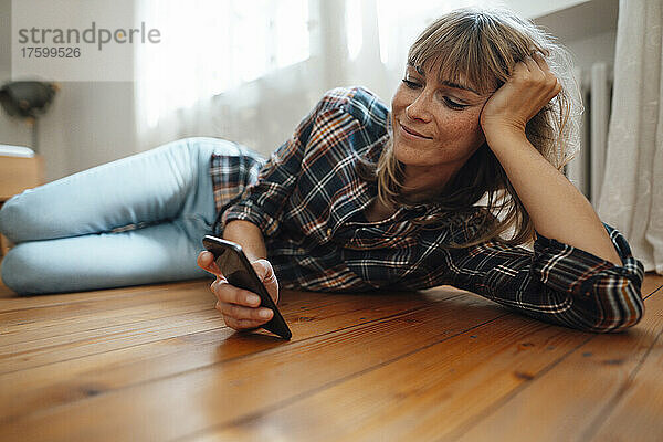 Frau mit Pony benutzt Smartphone zu Hause auf dem Boden