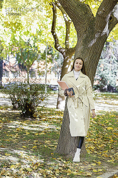 Junge Frau lehnt an Baum im College-Park