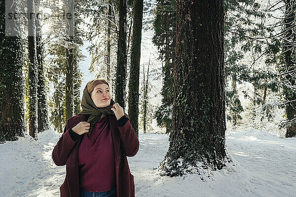 Nachdenkliche Frau mit Schal steht im Winterwald