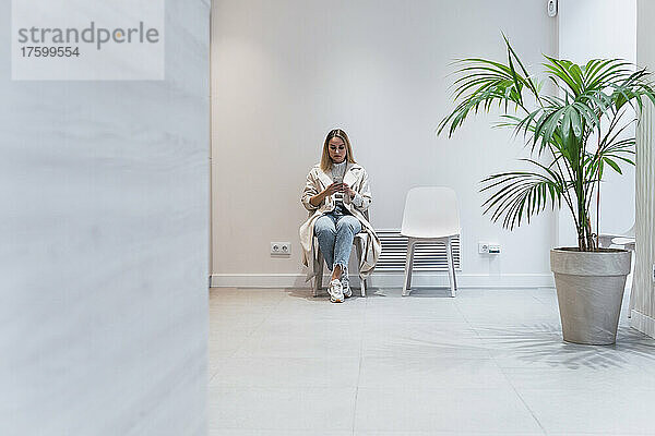 Junge Frau benutzt Mobiltelefon im Wartezimmer der Klinik