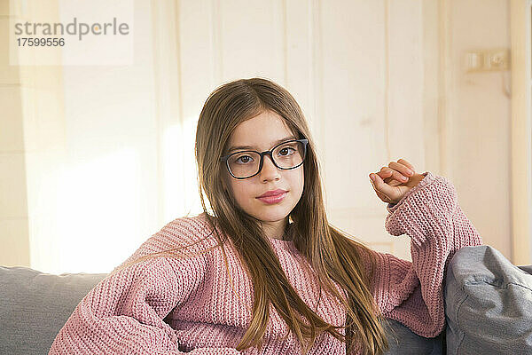 Vorpubertäres Mädchen mit Brille auf Sofa zu Hause
