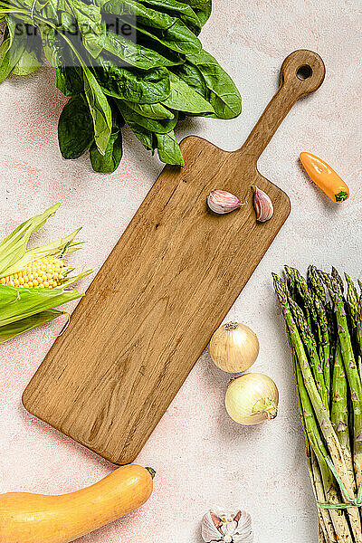 Studio shot of assorted vegetables surrounding cutting board