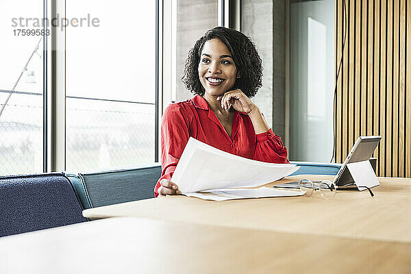 Lächelnde Geschäftsfrau mit Dokumenten am Arbeitsplatz