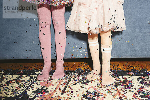 Legs of girls standing on floor covered with confetti